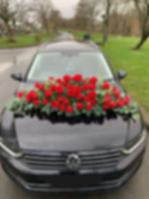 A hearse dressed with a bed of red silk roses on the bonnet